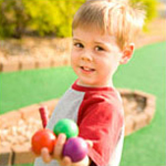young boy holding golf balls at miniature golf course