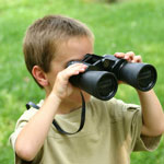 boy looking through binoculars in a green field